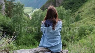 一位年轻的梦幻女子坐在群山的背景上，头发飞扬。 慢动作